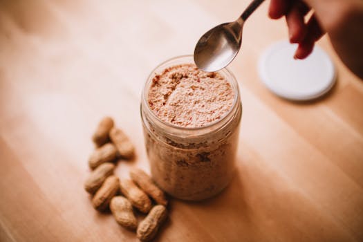 A glass jar of homemade peanut butter on a wooden table with peanuts and a spoon.